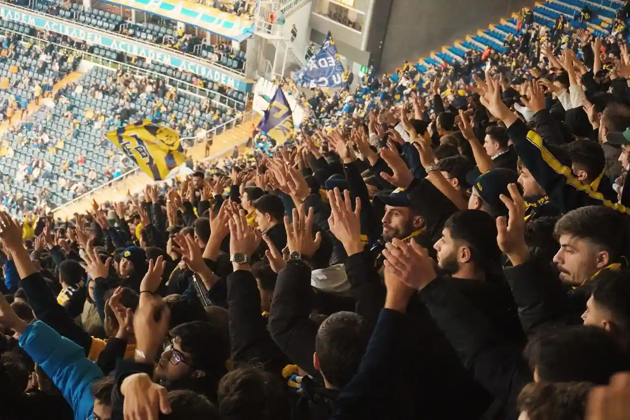 Supporters de football mains levées qui acclament leur équipe dans les tribunes d'un stade