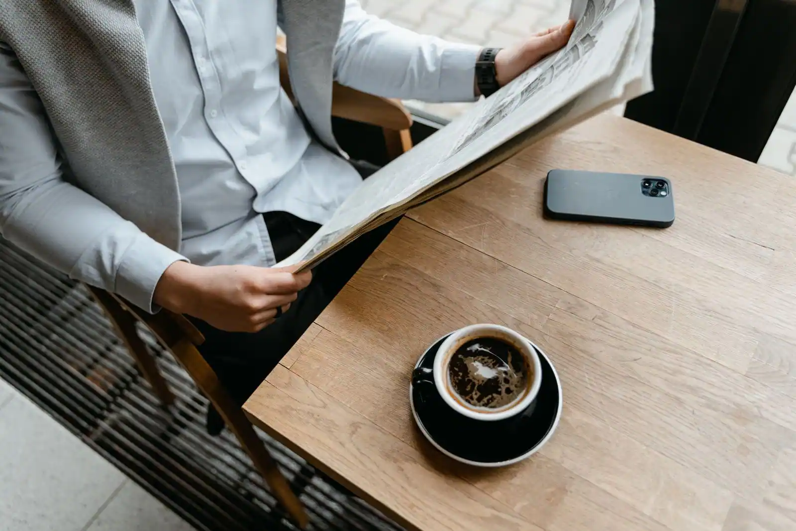 Personne lisant un journal à une table, un smartphone et une tasse de café posés à côté