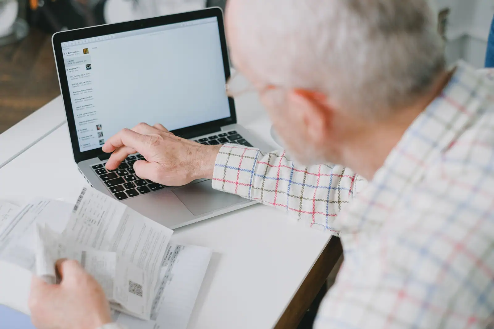 Personne consultant ses comptes en ligne sur un ordinateur portable, des relevés papier à la main.