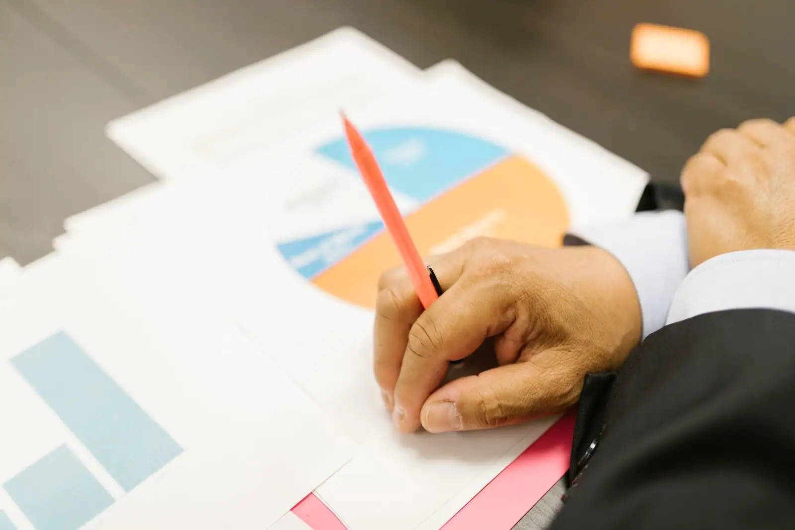Main d'une personne en costume annotant au stylo des documents financiers à graphiques
