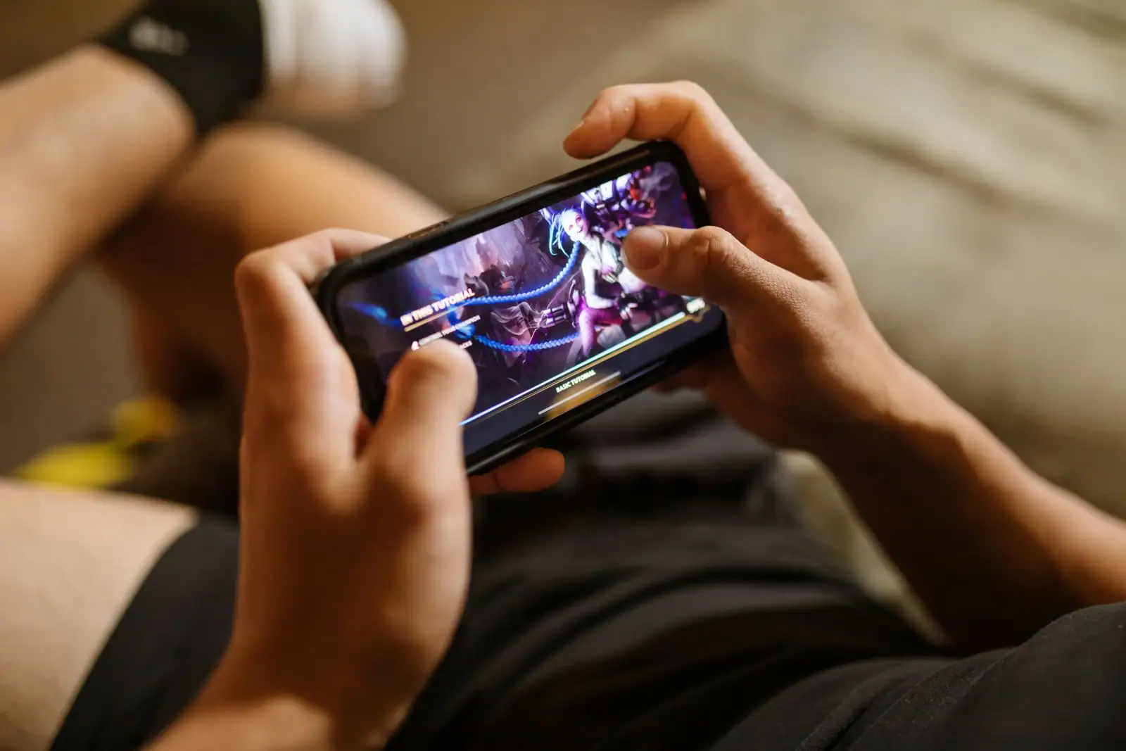 Personne tenant un smartphone à deux mains et jouant à un jeu vidéo mobile coloré.