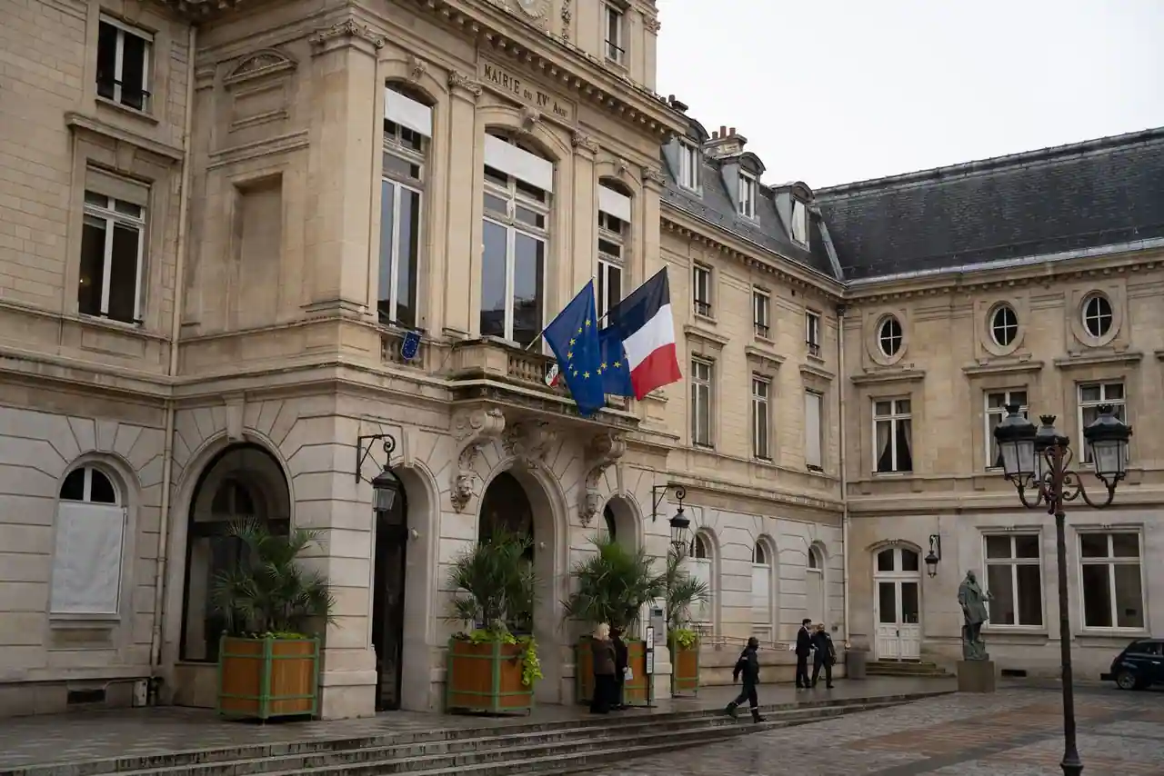 Façade d'une mairie d'arrondissement parisienne avec les drapeaux français et européen à l'entrée