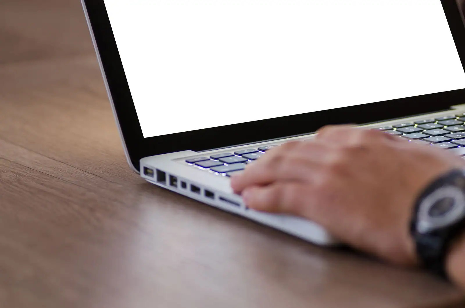 Main tapant sur le clavier d'un ordinateur portable posé sur un bureau en bois, écran vierge