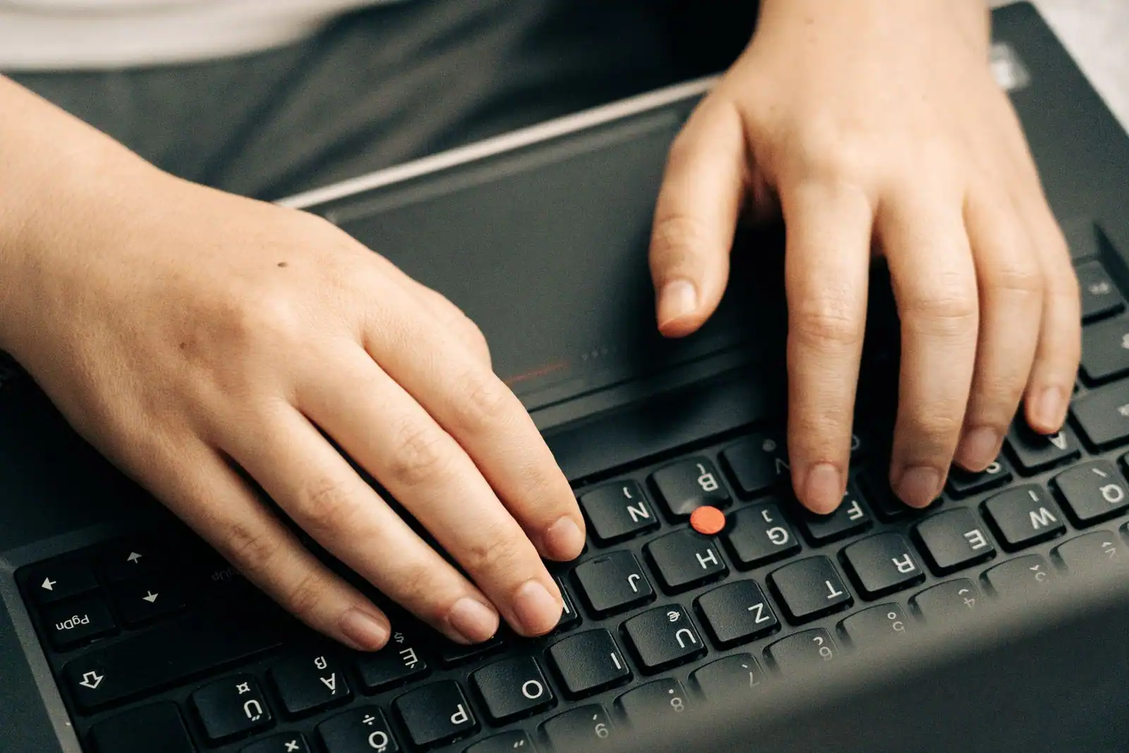 Des mains tapent sur le clavier noir d'un ordinateur portable