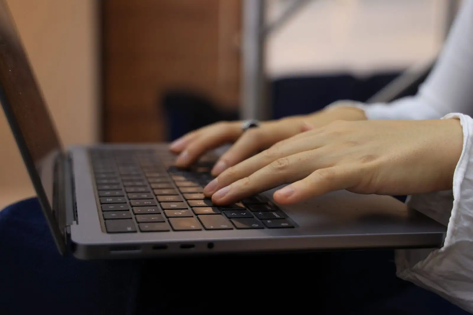 Les mains d'une personne tapent sur le clavier d'un ordinateur portable posé sur ses genoux.