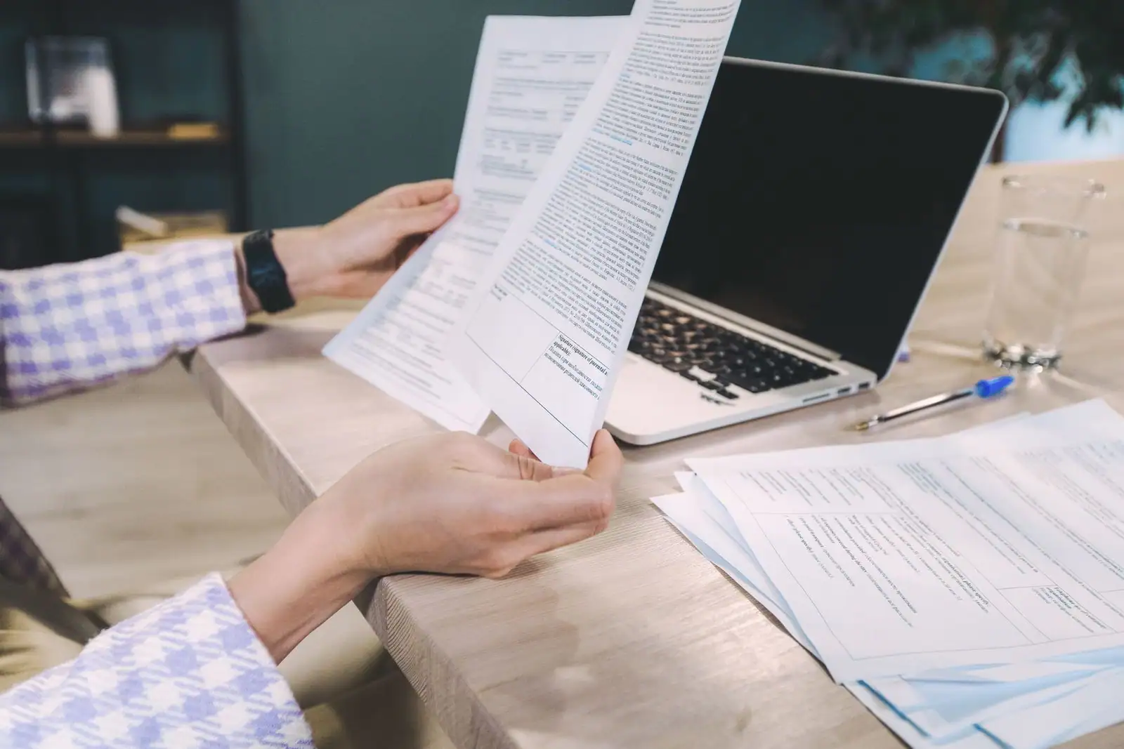 Personne lisant des documents financiers imprimés à un bureau, avec un ordinateur portable