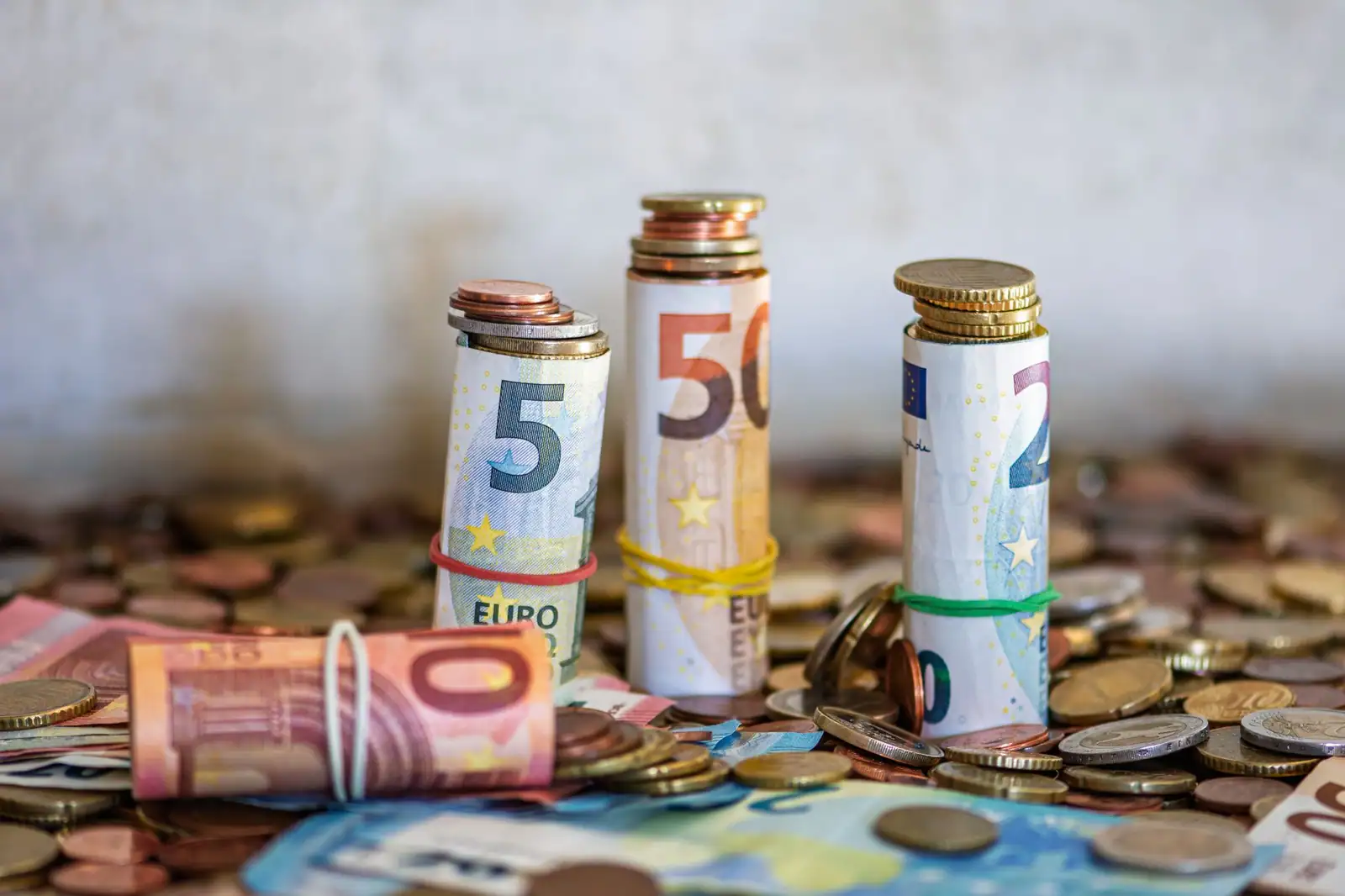 Rouleaux de billets en euros maintenus par des élastiques, posés sur un tas de pièces en euros