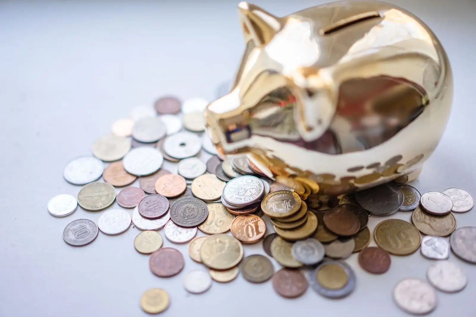 Tirelire dorée en forme de cochon entourée de pièces de monnaie variées, sur une surface claire