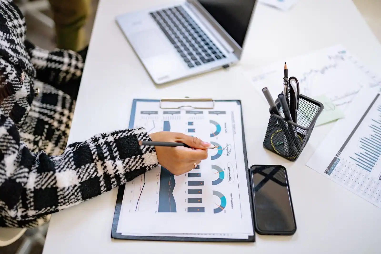 Personne examinant des graphiques financiers au stylo, ordinateur portable et smartphone posés sur le bureau