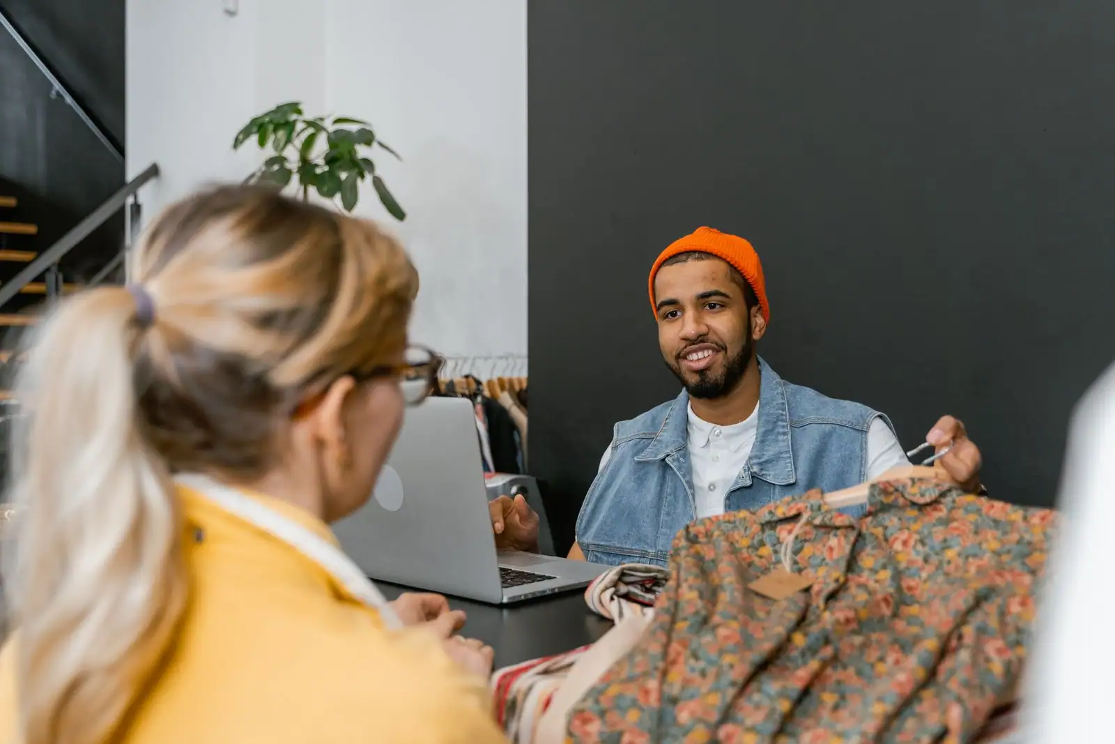 Vendeur souriant conseillant une cliente qui examine un vêtement au comptoir d'une boutique