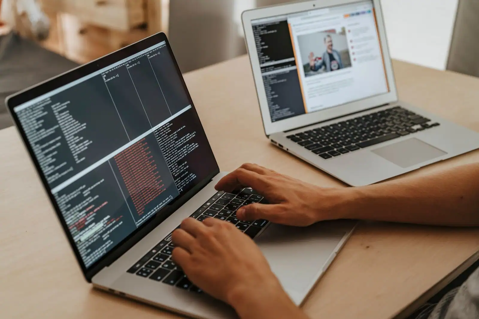 Mains tapant du code sur un ordinateur portable, devant un second écran affichant une page web.