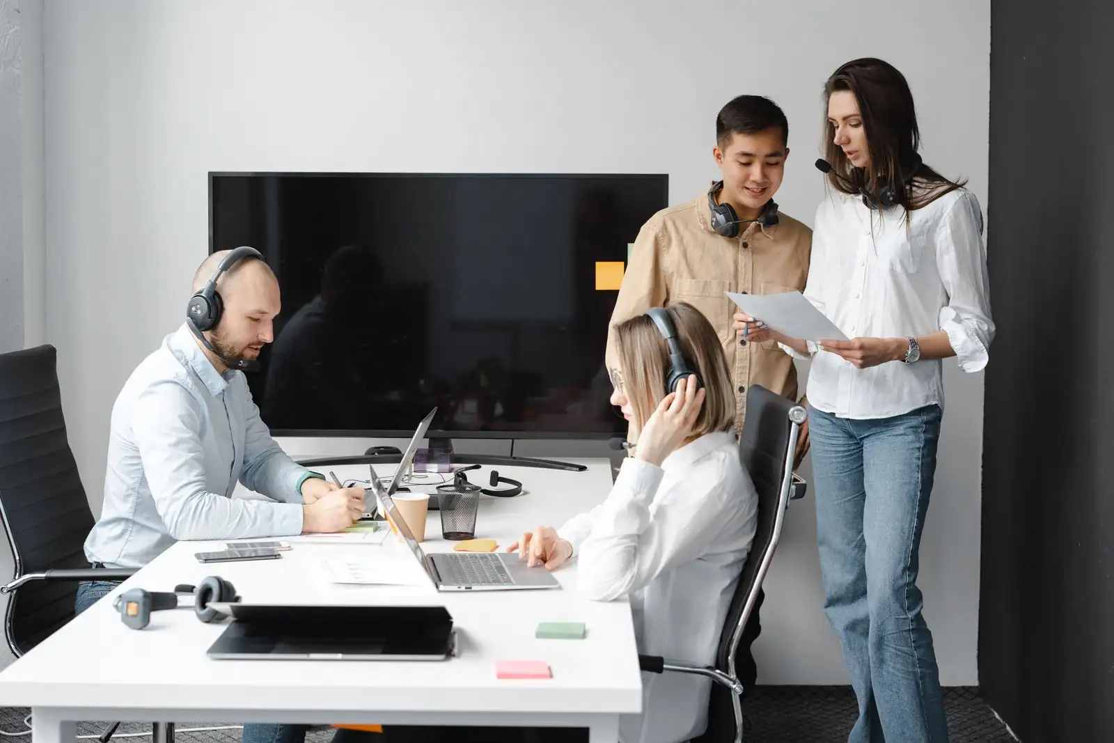 Quatre collègues réunis autour d'un poste de travail avec ordinateurs portables dans un open space lumineux