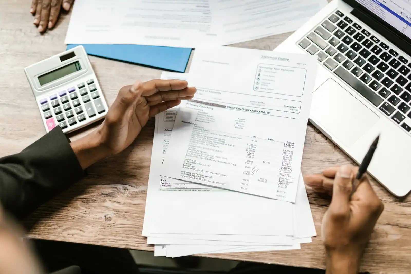 Une personne examine des documents financiers à un bureau, avec une calculatrice, un ordinateur portable et un stylo.