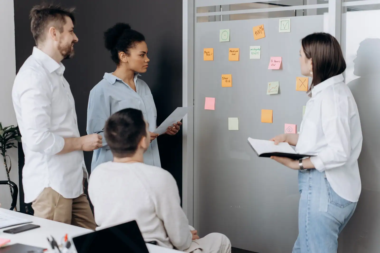 Équipe réunie autour d'un tableau couvert de notes adhésives colorées, échangeant lors d'une réunion de travail