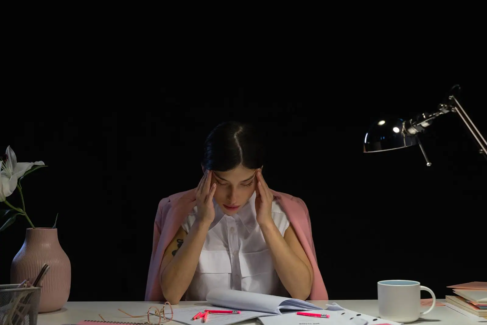 Femme assise à son bureau, les mains sur les tempes, dans une ambiance de travail pesante