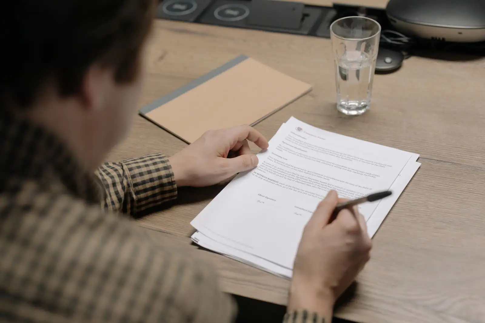 Personne examinant et signant un document de contrat imprimé, stylo à la main, sur un bureau en bois.