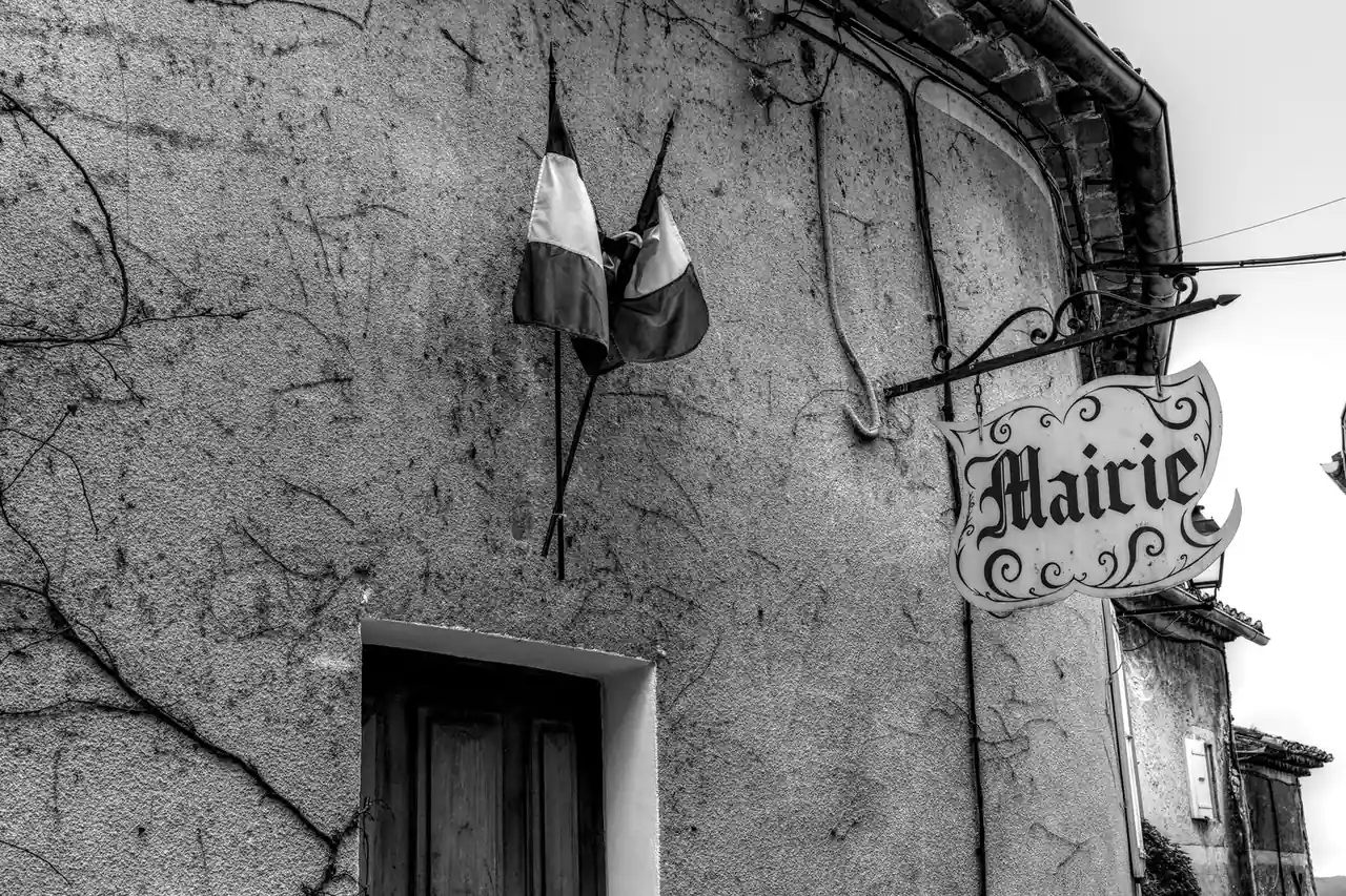 Façade d'une mairie française avec drapeaux tricolores et enseigne « Mairie », photo en noir et blanc