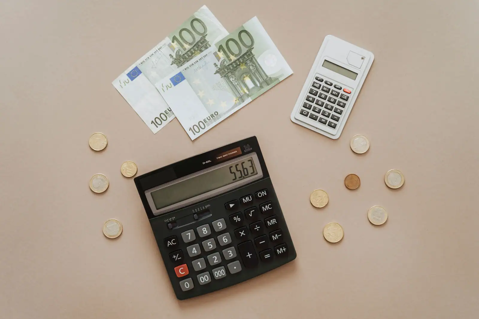 Billets de cent euros, pièces de monnaie et deux calculatrices posés sur un fond beige