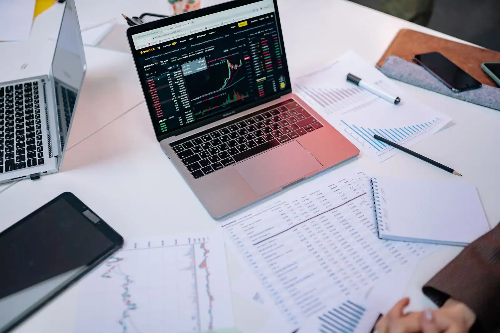 Ordinateur portable affichant un graphique de cours de Bourse, entouré de documents financiers et d'un carnet