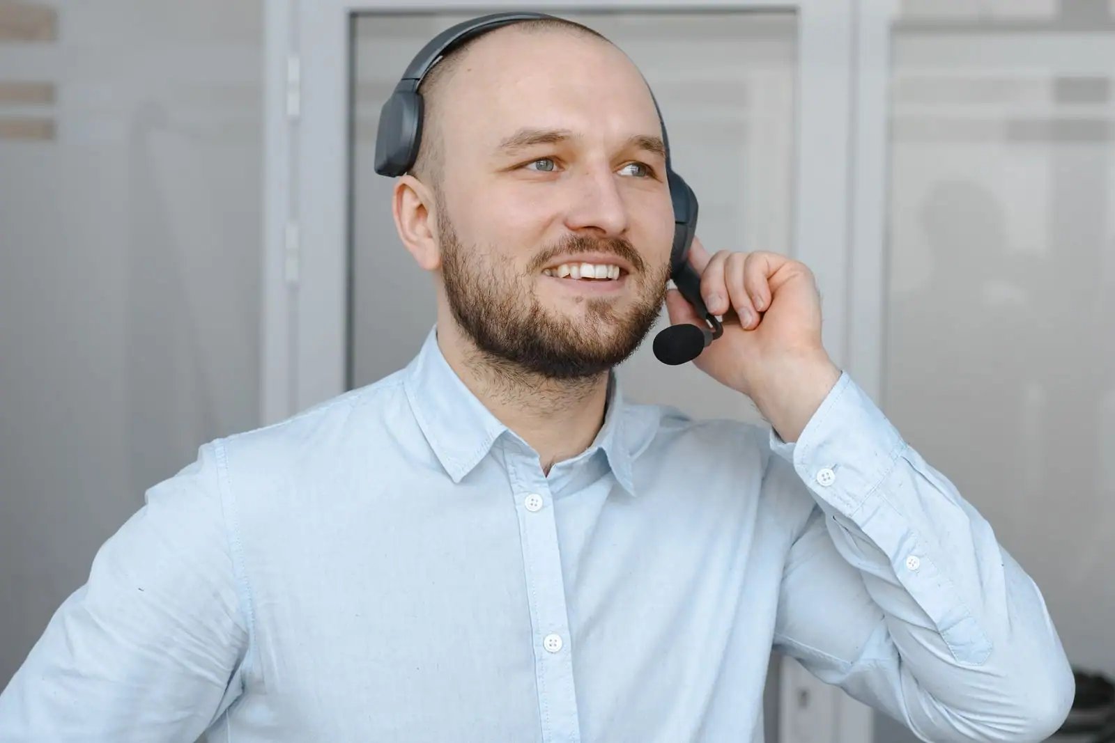 Conseiller souriant portant un casque-micro, en chemise claire, dans un bureau lumineux