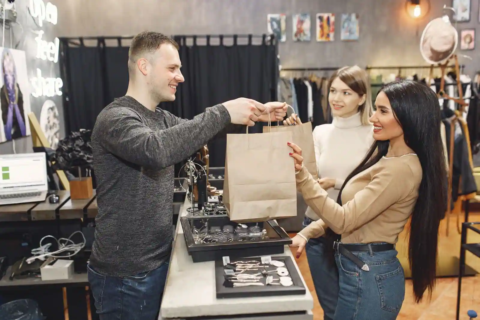Vendeur souriant remettant un sac à des clientes satisfaites au comptoir d'une boutique