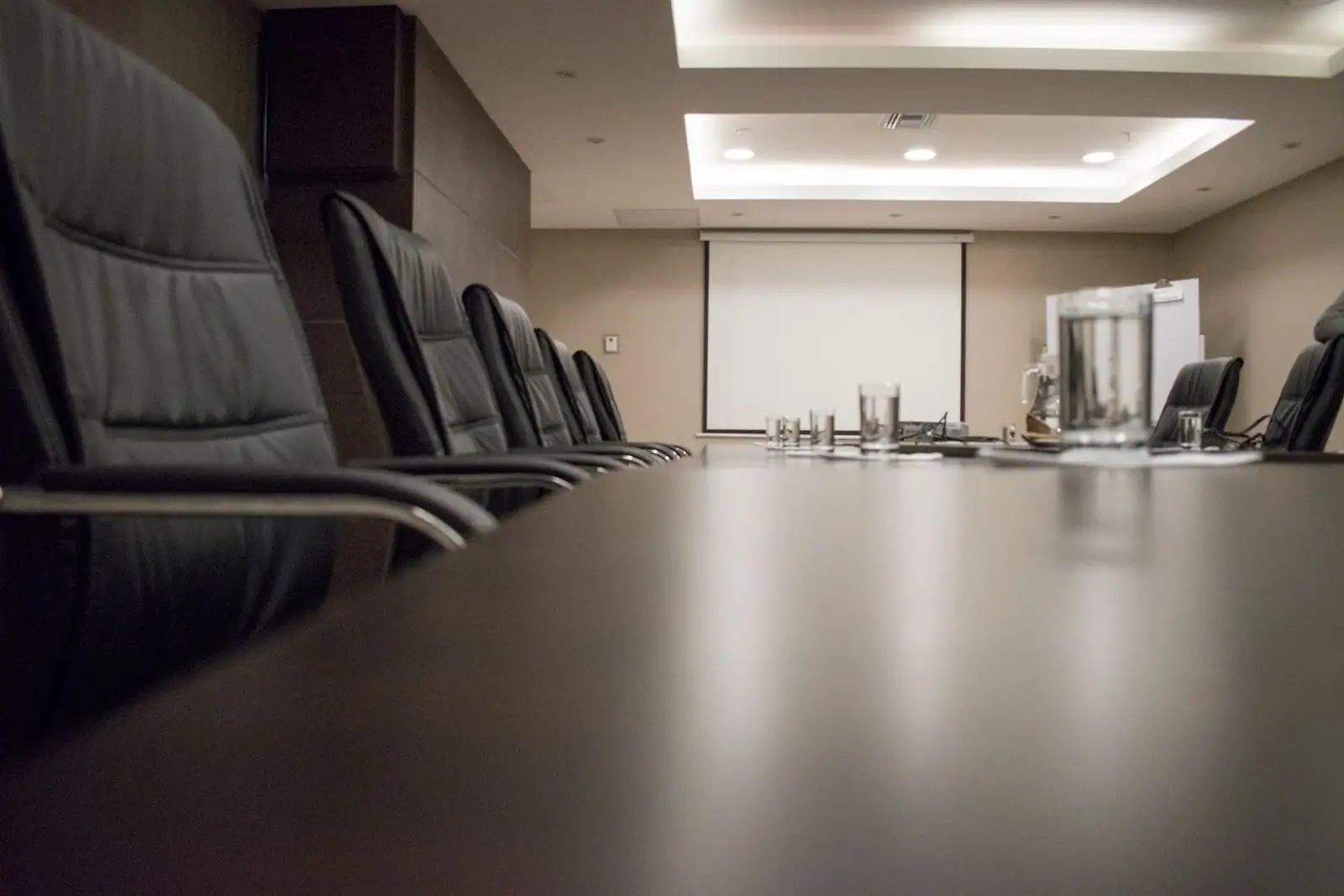 Salle de conseil vide : longue table sombre, sièges en cuir alignés et écran de projection