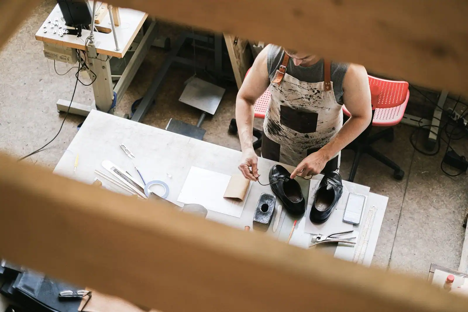 Vue plongeante sur un artisan en tablier travaillant une paire de chaussures en cuir sur son établi