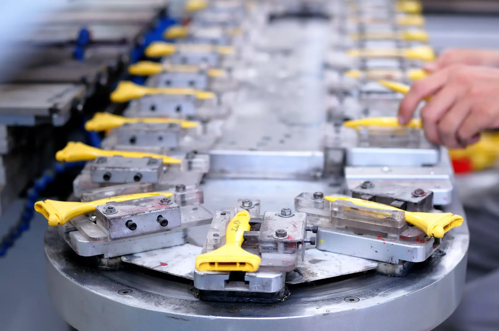 Pièces métalliques et pinces jaunes alignées sur une ligne de production industrielle, main d'un opérateur