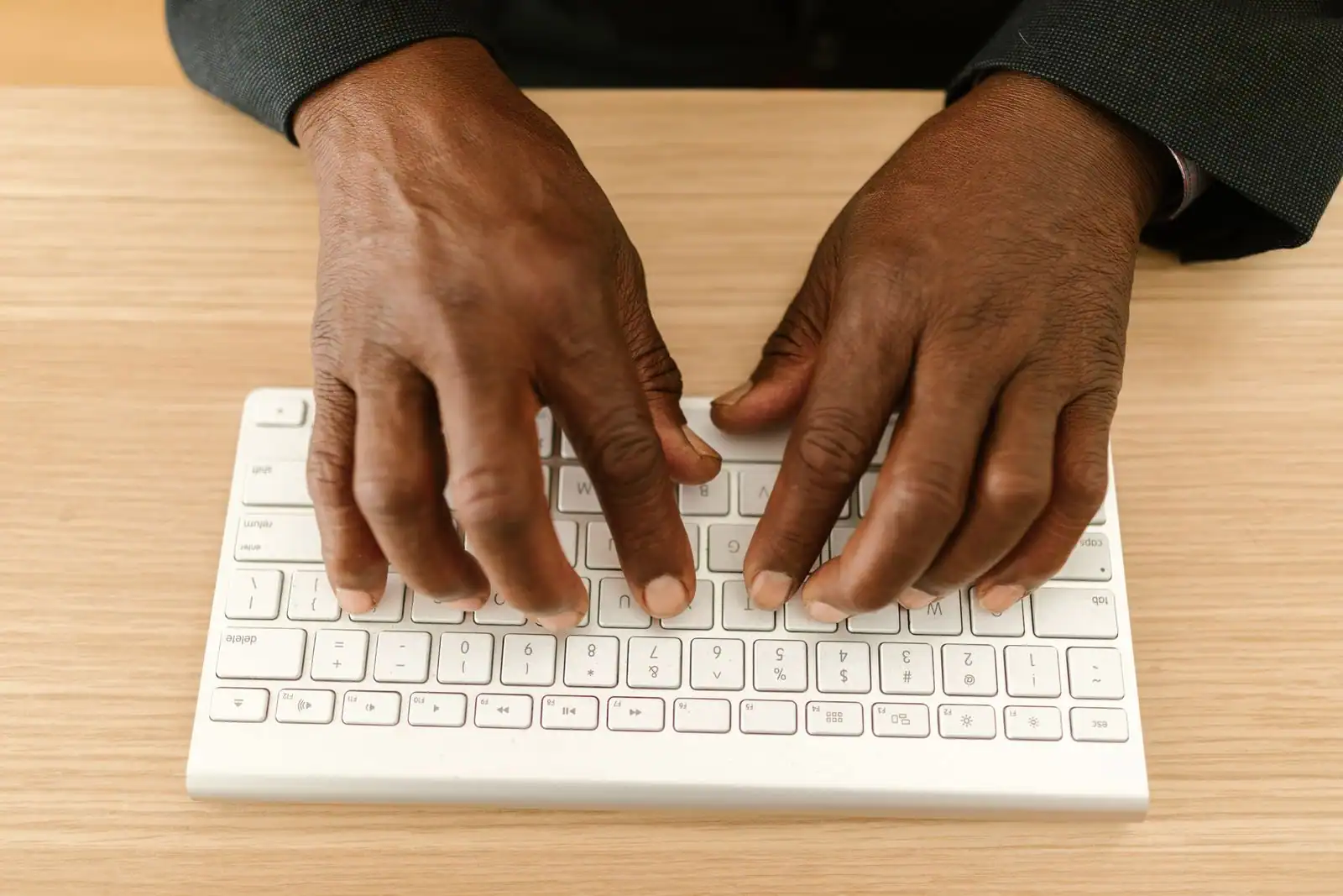 Deux mains en gros plan tapant sur un clavier d'ordinateur blanc, posé sur un plan de travail en bois clair.