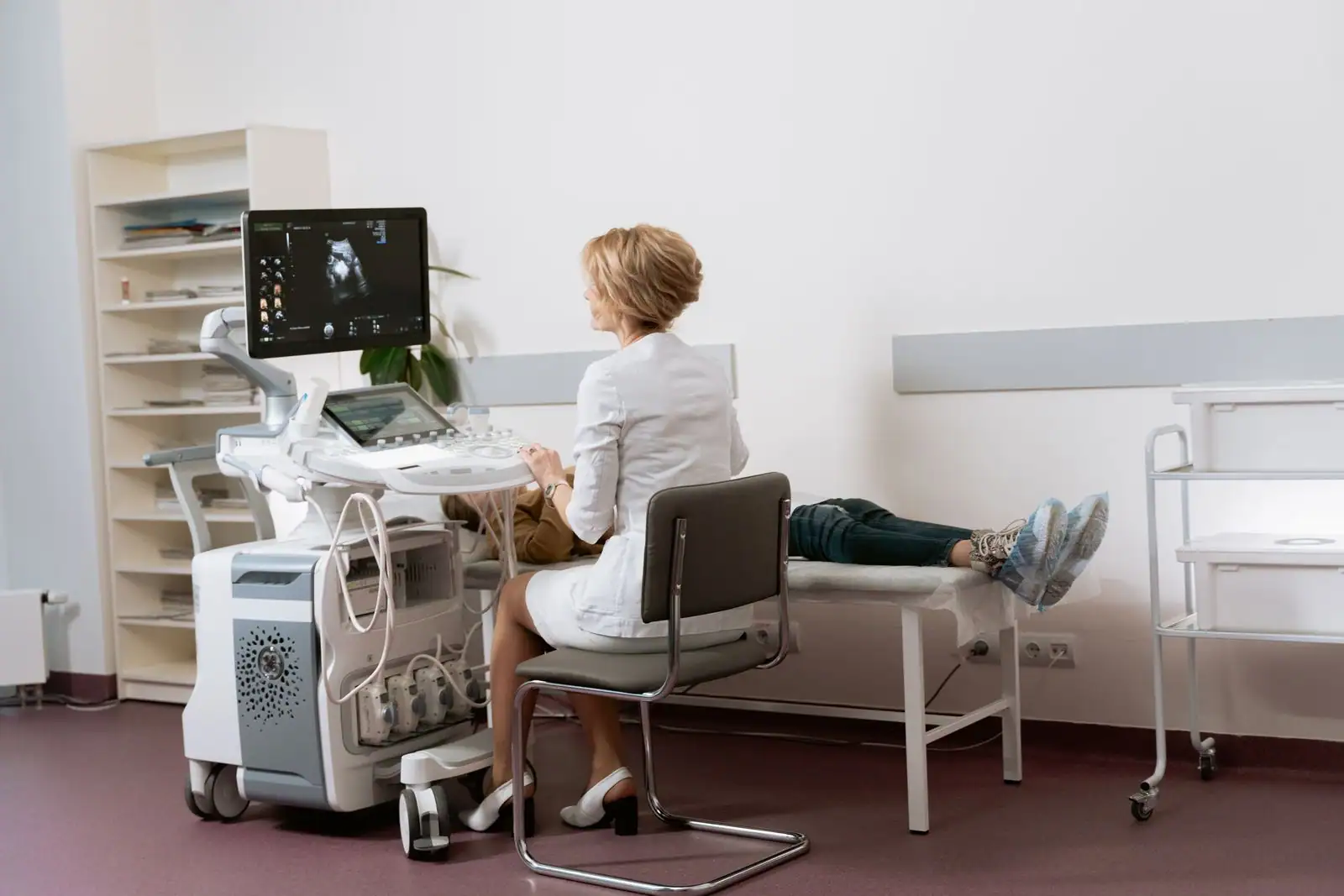Salle d'échographie médicale : une praticienne manipule l'appareil pendant l'examen d'une patiente allongée.
