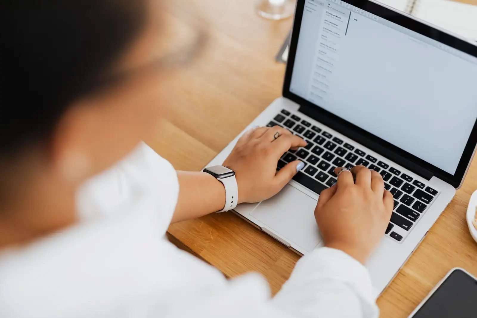 Vue de dessus : une personne tape sur le clavier d'un ordinateur portable posé sur une table en bois.