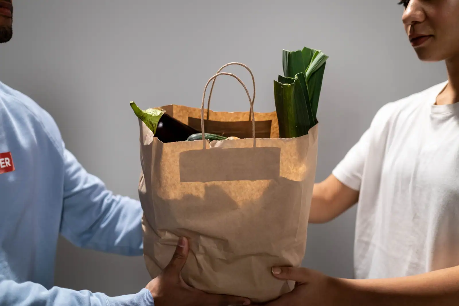 Deux personnes se passent un sac en papier rempli de légumes lors d'une distribution alimentaire.