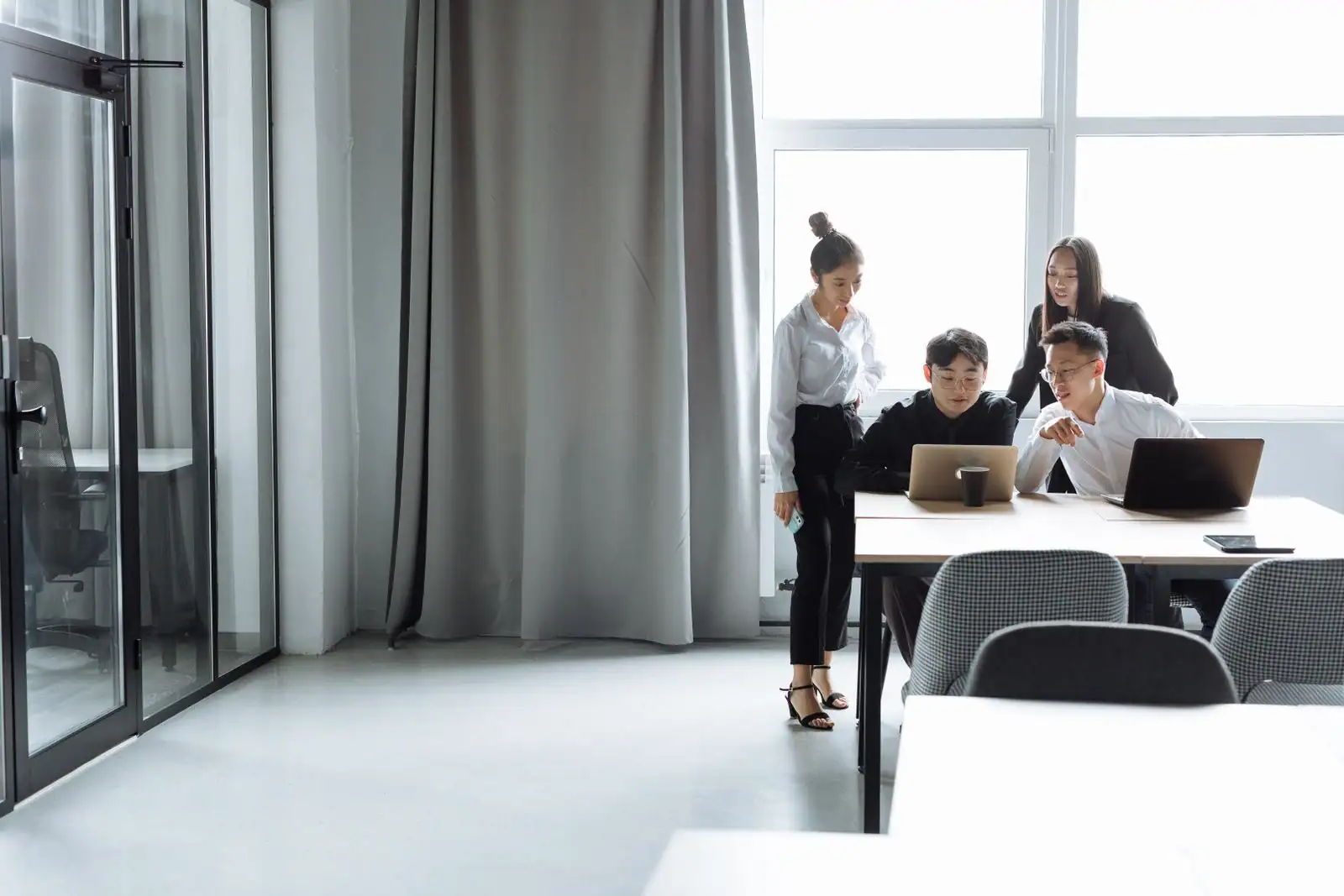 Quatre collègues rassemblés autour d'une table de bureau, penchés vers deux ordinateurs portables