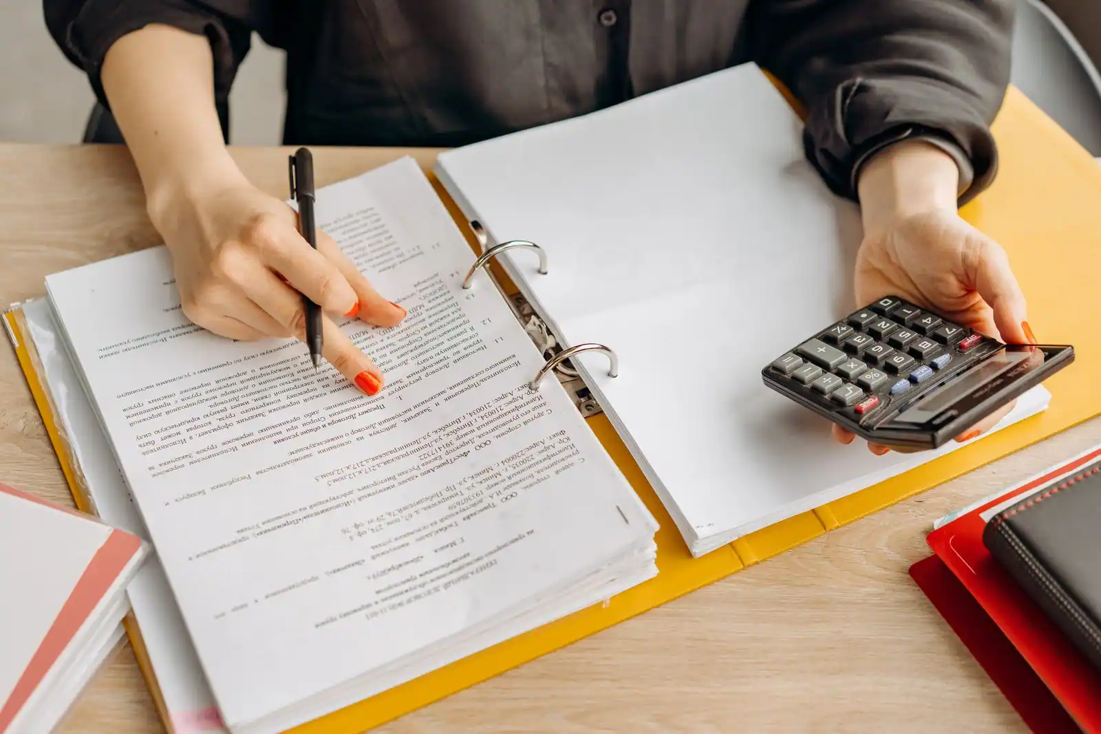 Classeur de documents ouvert sur une table, stylo à la main et calculatrice, tri de papiers administratifs.