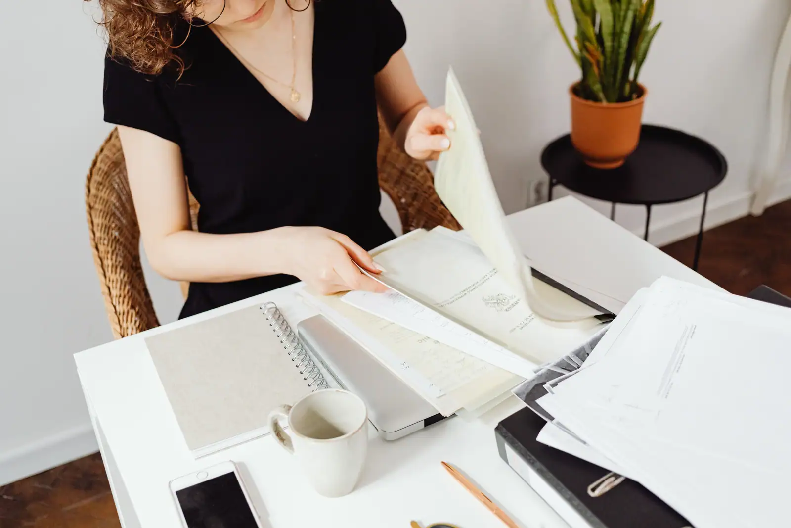 Une femme feuillette une pile de documents papier posés sur une table, sans texte lisible à l'image