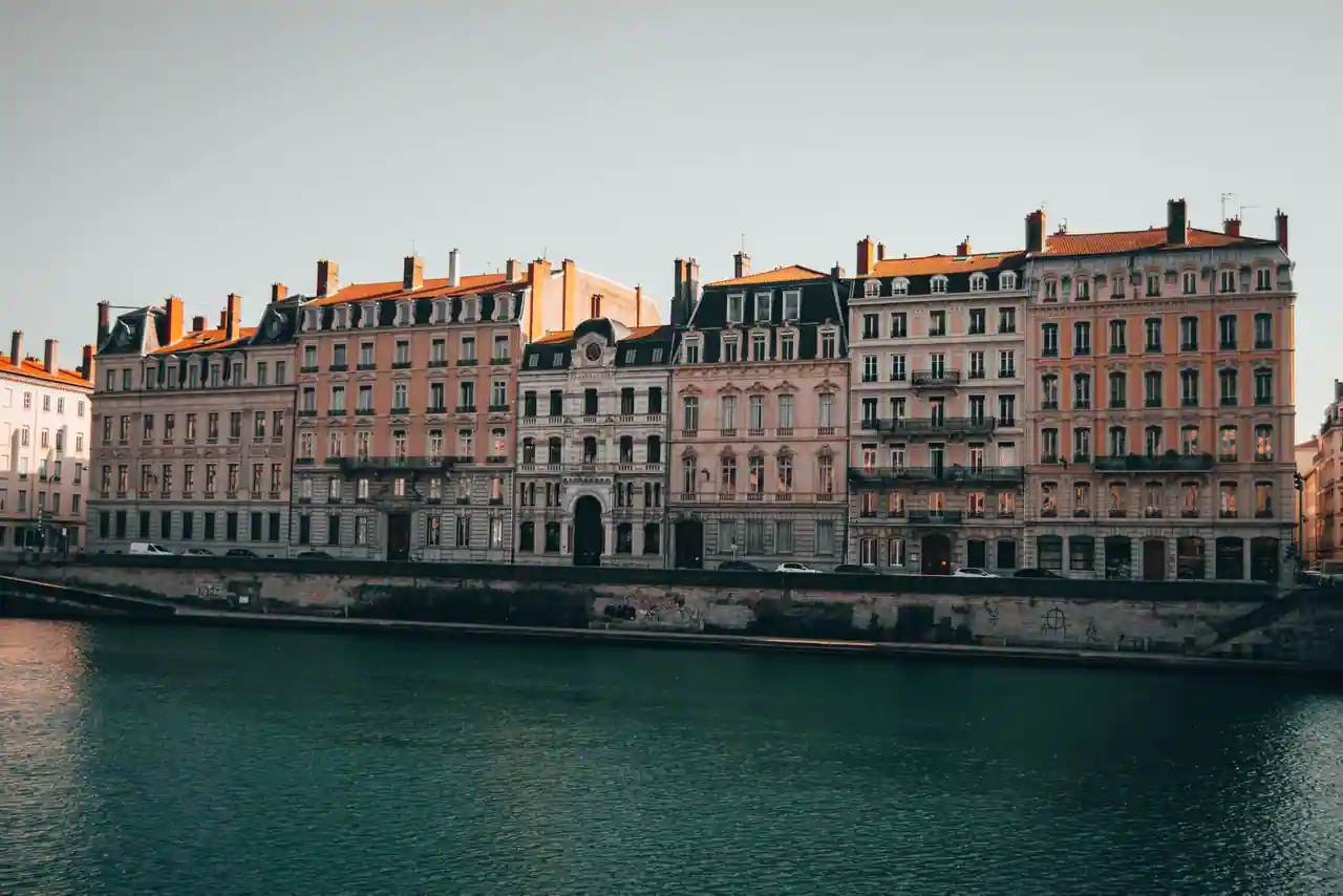 Immeubles anciens alignés le long des quais d'un fleuve à Lyon, façades claires en fin de journée