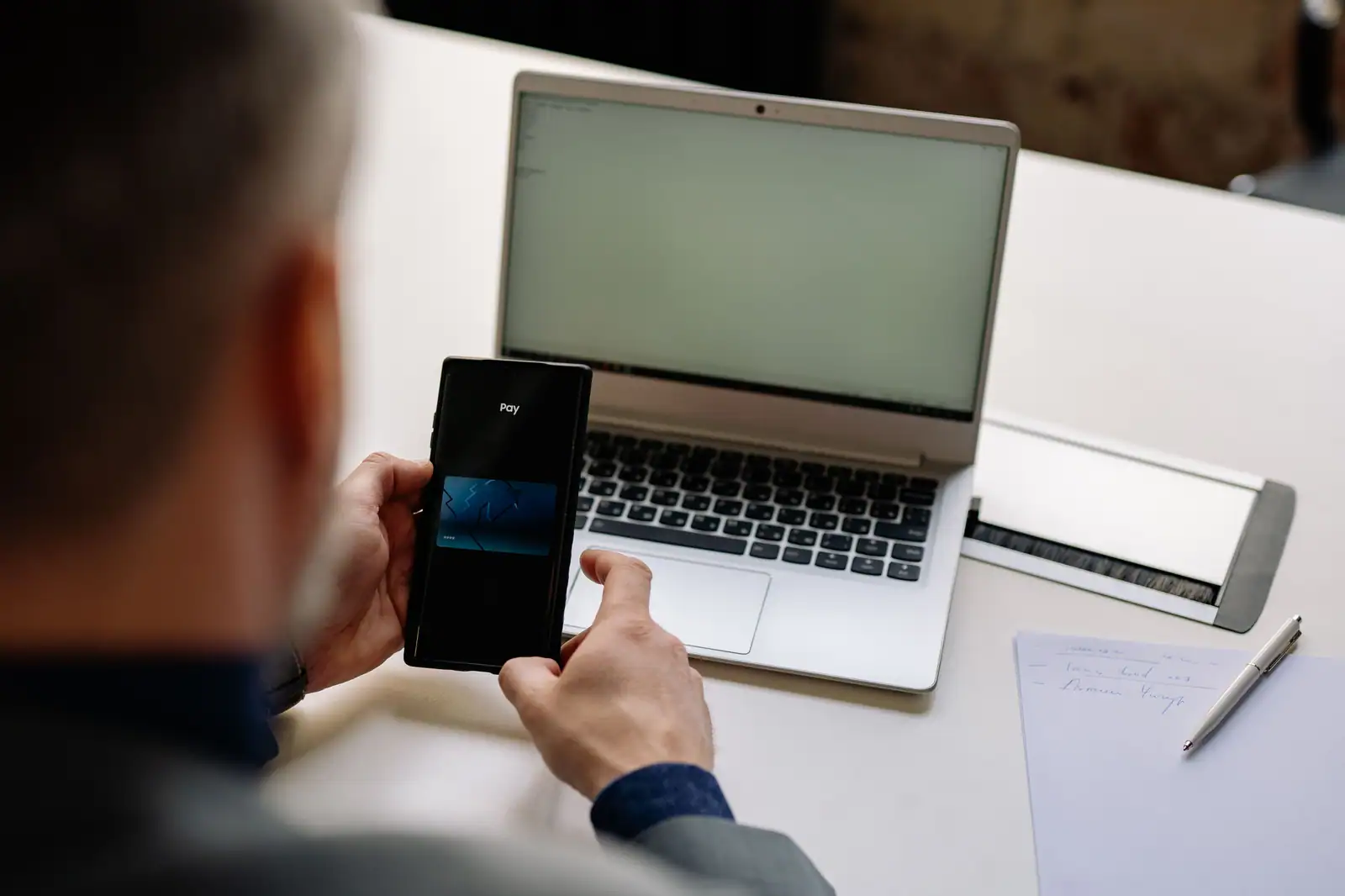Homme validant une opération de paiement sur son téléphone, devant un ordinateur portable ouvert