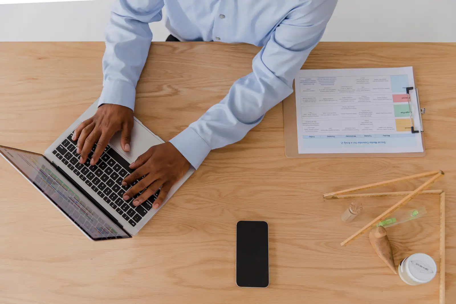 Personne travaillant sur un ordinateur portable à un bureau, avec un smartphone et des documents à proximité.