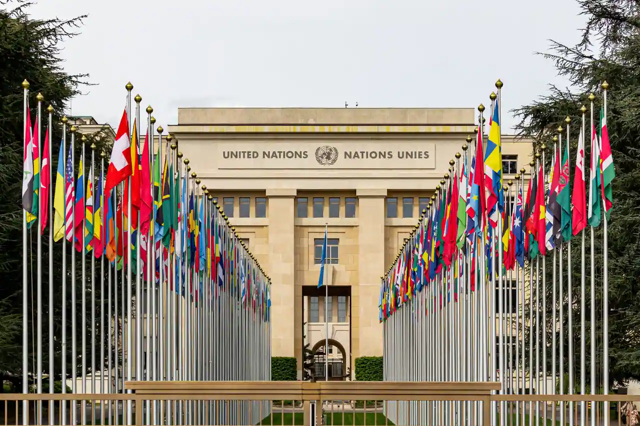 Façade de l'Office des Nations unies à Genève, bordée par l'allée des drapeaux des pays membres.