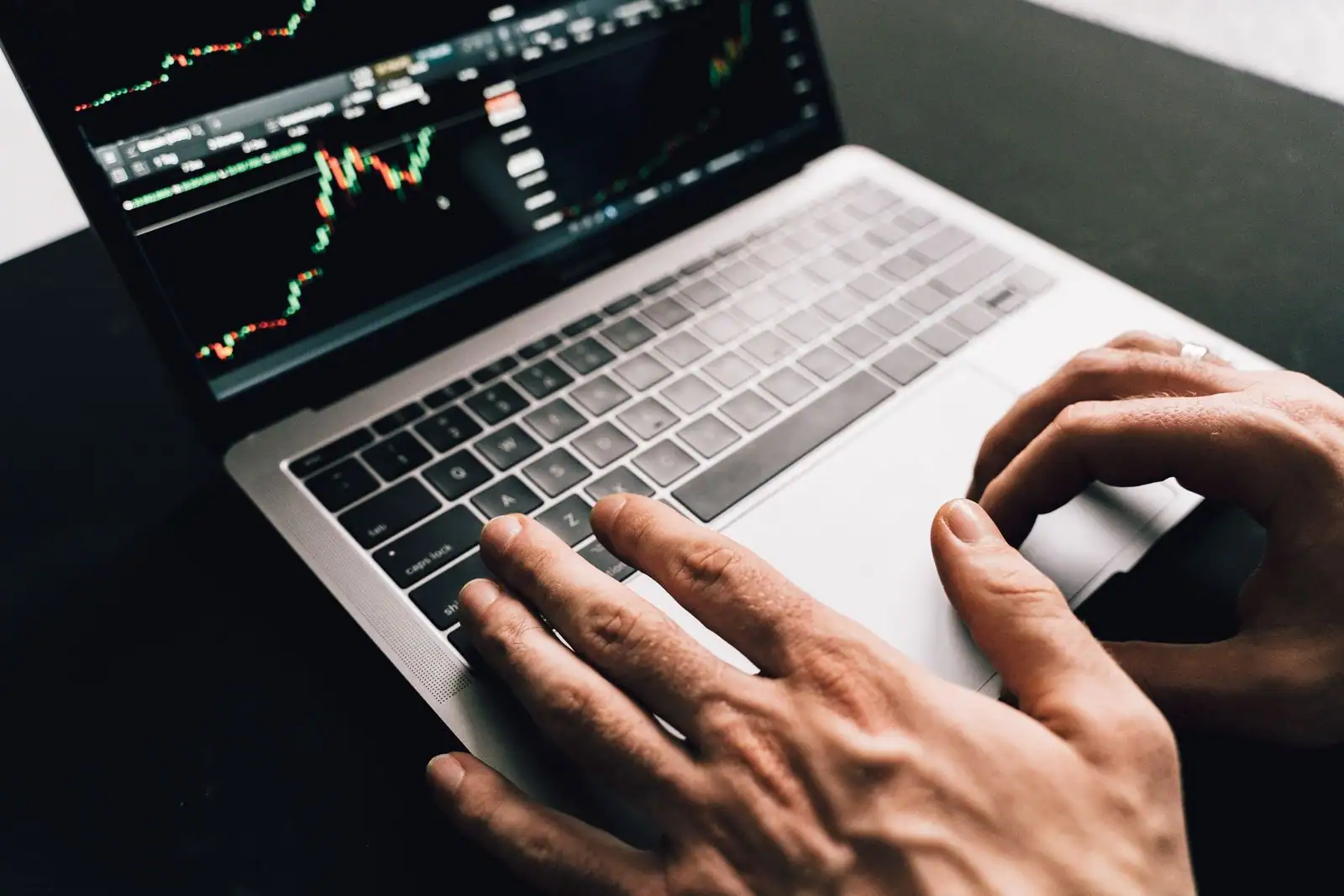 Mains sur le clavier d'un ordinateur portable, écran affichant un graphique financier.